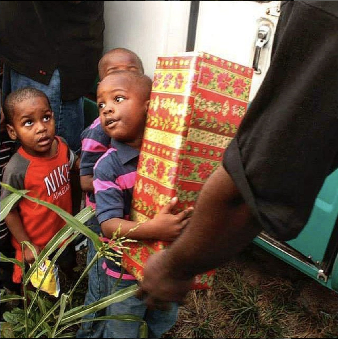Two young boys with curious expressions looking at a person holding a decorated Christmas gift box.