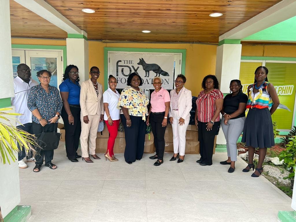 Group of women standing together in front of a sign for the Fox Foundation, with some people wearing business casual and others in semi-formal attire.